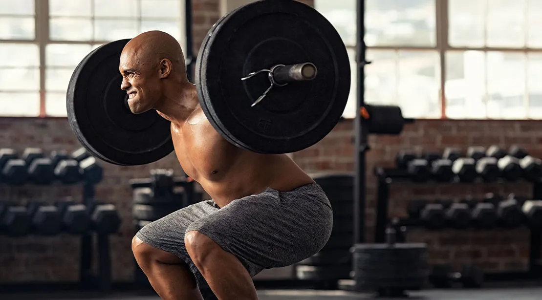 Bald muscular man performing a barbell back squat for his lower back strength training workout