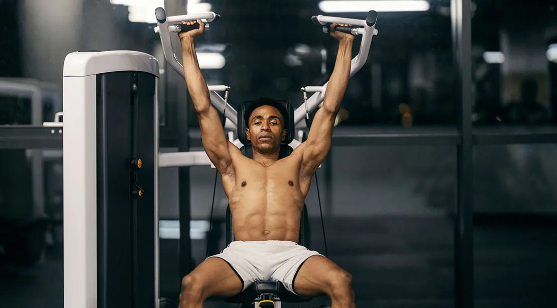 Fit athletic man performing a Seated Shoulder Press using a machine